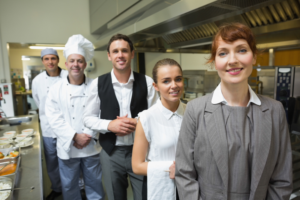 Nice female manager posing with the staff in a professional kitchen