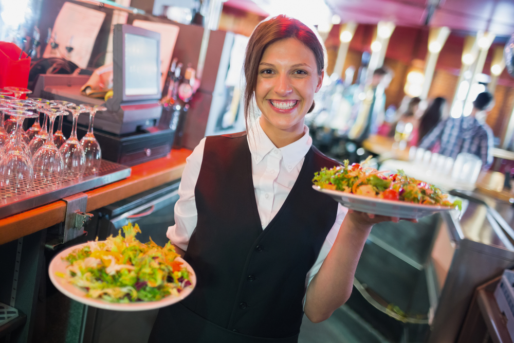 Pretty lady holding plates of salads in a bar