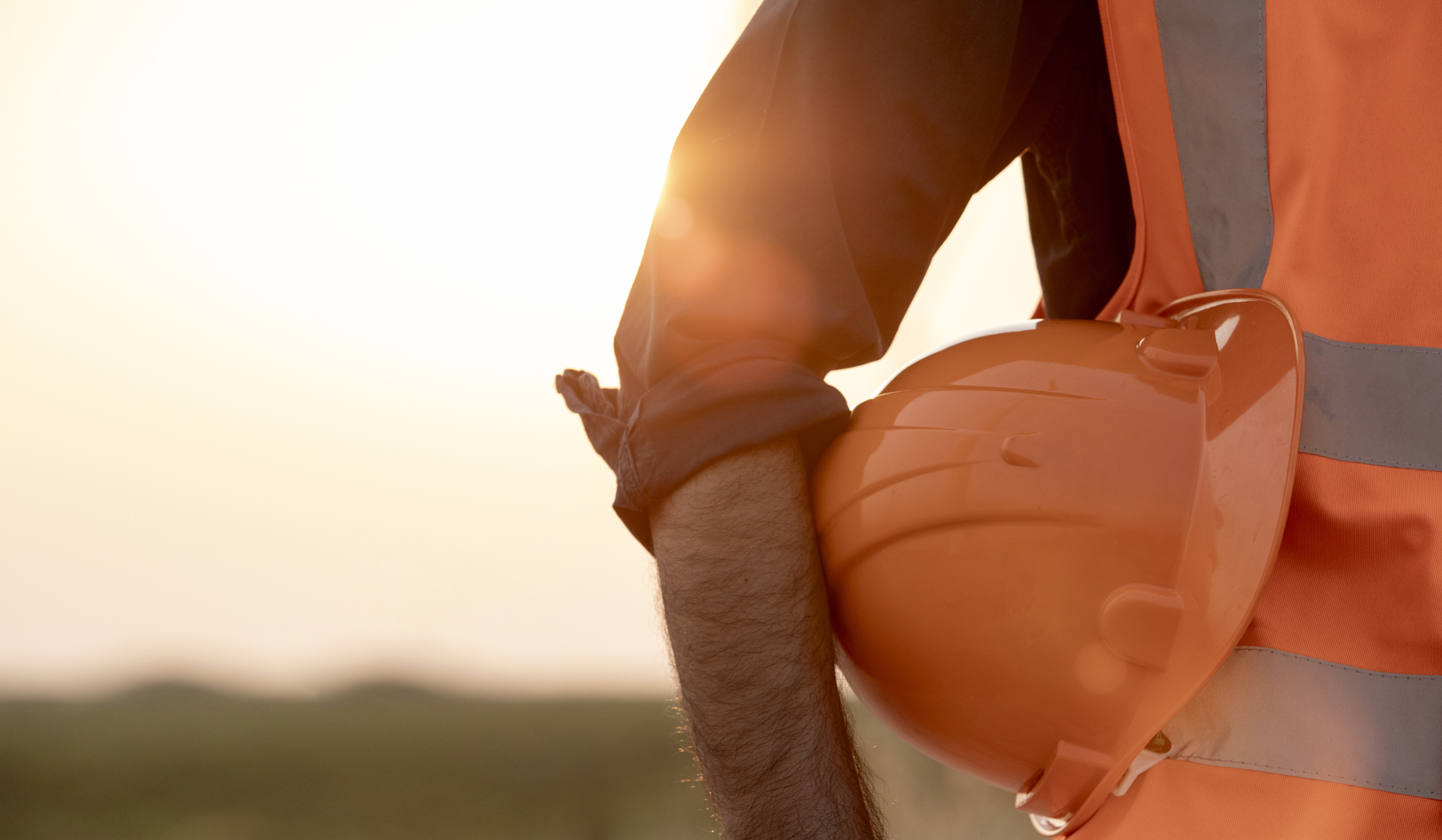 Worker holding orange hard hat at sunset